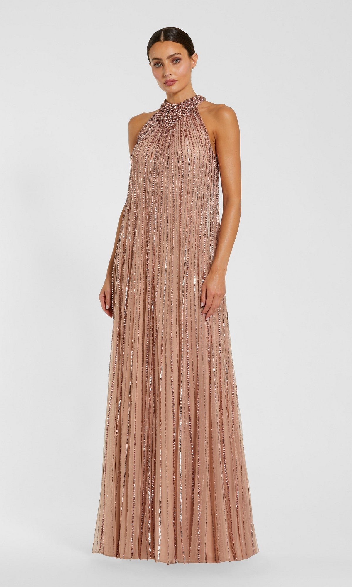 A woman wearing the Mac Duggal 23043 long formal dress in rose gold, featuring a sleeveless design and vertical sequin detailing, stands against a plain white background.